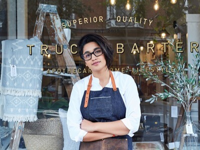 A business owner, probably a coffee shop, standing in front of her store with her arms crossed