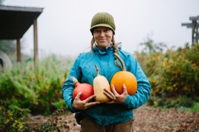 A woman hold three large pumpkin-like vegetables in her arms