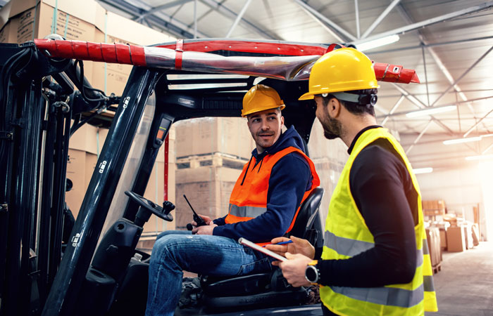 A man in forklift talking to a man with a clipboard