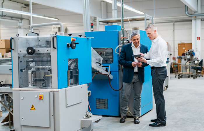 Two employees working on a tablet near industrial machinery