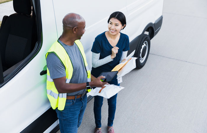 A delivery driver in hi-vis safety vest handing off a delivery to an employee