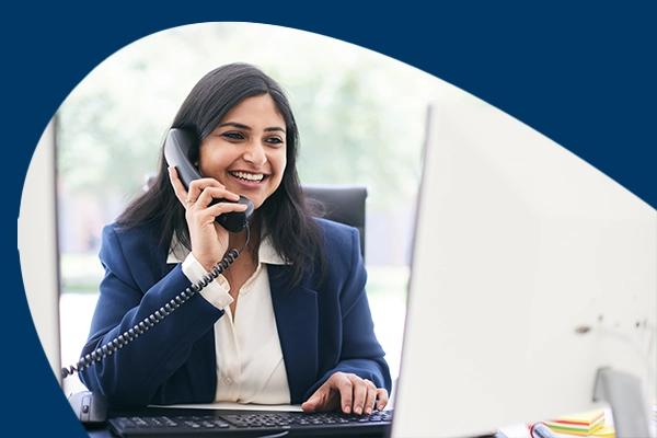 A happy woman talking on the phone while working on the computer
