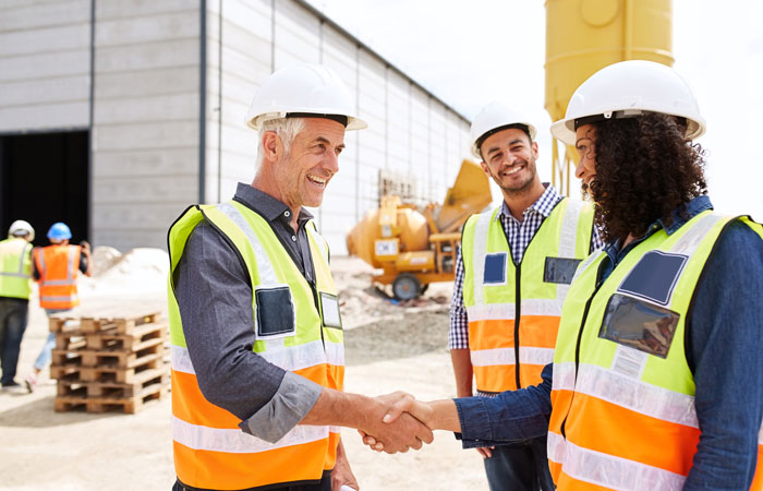 People in hi-viz vest and hard hats shaking hands in front of a warehouse