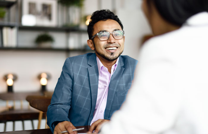 A man in a suit with glasses smiling at the person he's meeting with
