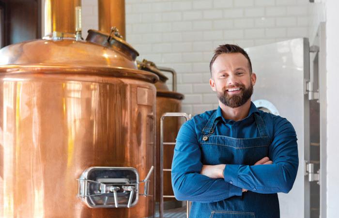 A brewer posing in front of a brewery tank