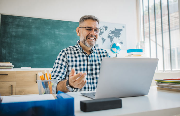 A teacher sitting in their classroom working on their laptop