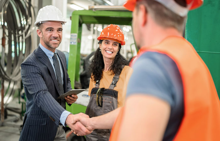 A man in a suit and a hard hat shaking hands with two warehouse workers