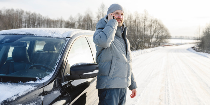 driver standing on the side of a snow-covered road talking on his phone