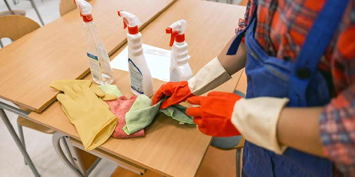 person wearing rubber gloves and cleaning school desks
