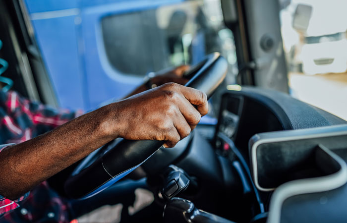 A close-up of a driver's hands holding on to a steering wheel of a truck