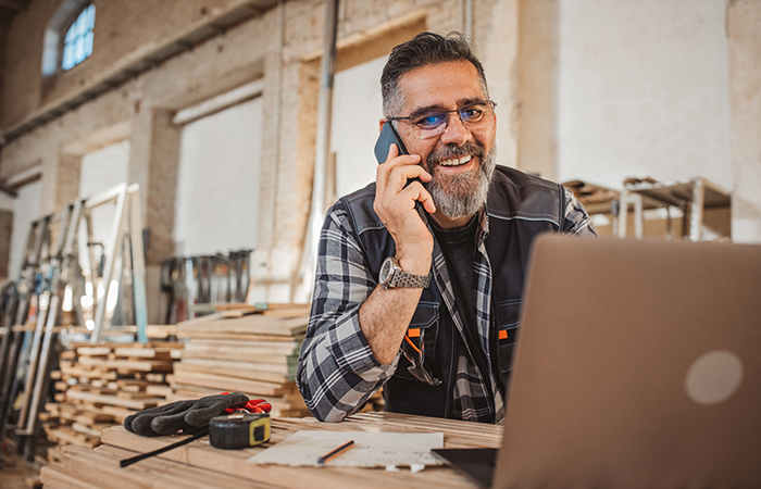 A man at a worksite on the phone working on his laptop
