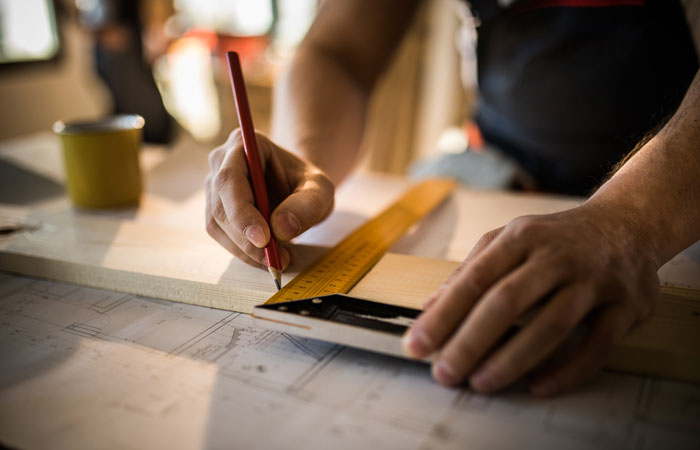 A close up shot of a wood worker marking a piece of material for cutting