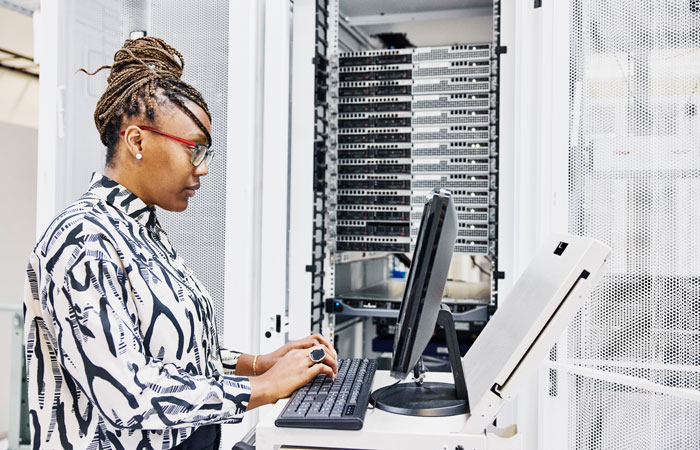 A woman working on a computer next to a server tower