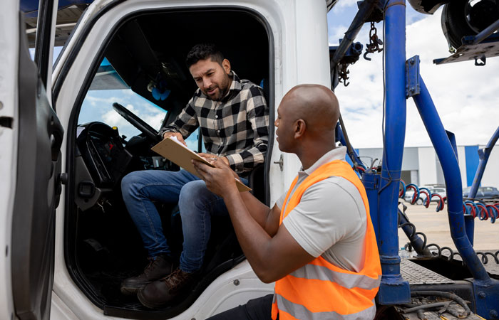 a truck driver signing something on a clipboard that is being held by a person in a hi-viz orange safety vest