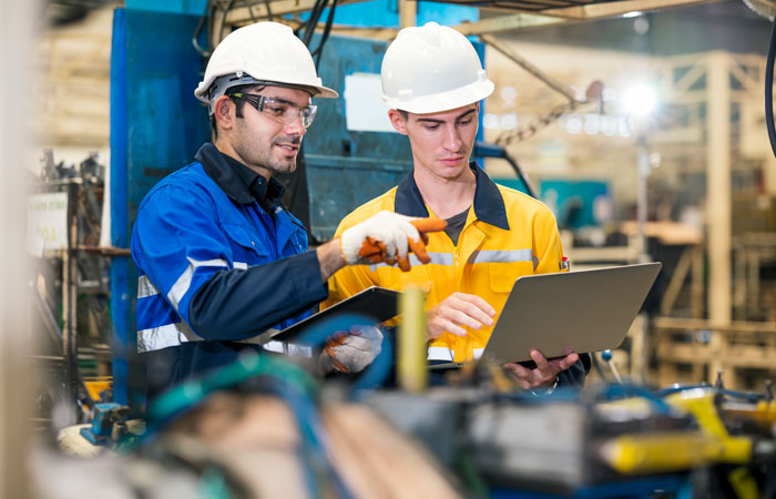 Two warehouse workers on a laptop working near machinery