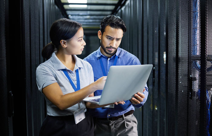 Two people working on a laptop in a server room