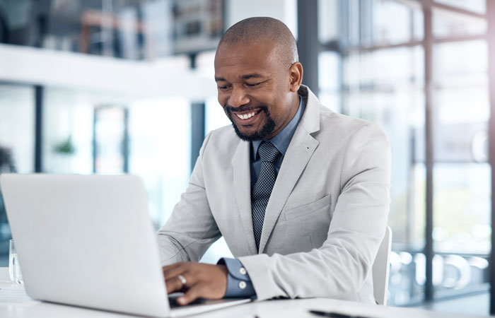 A man in a suit smiling working at a computer