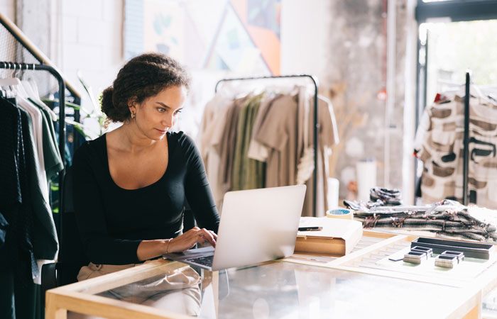 A woman in a clothing store working on a laptop