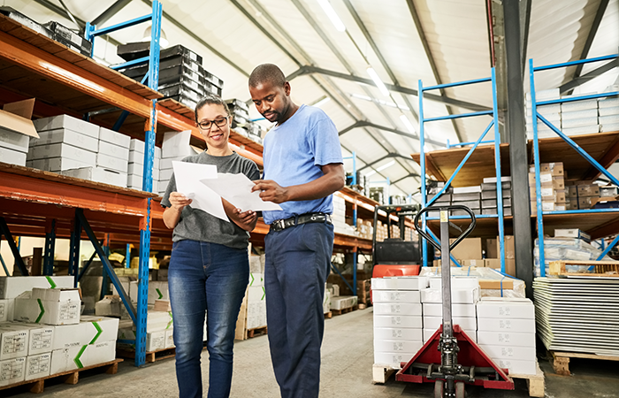 Two workers in a warehouse looking at paperwork