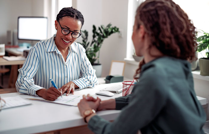 Two women sitting at a desk filling out paperwork