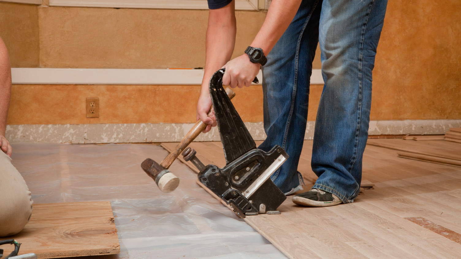 Person installing hardwood flooring with mallet and nailer