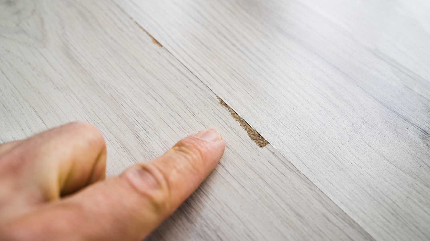 Person pointing out chipped part of wood floor